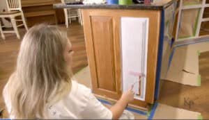 Painter rolling primer onto oak cabinet frames.